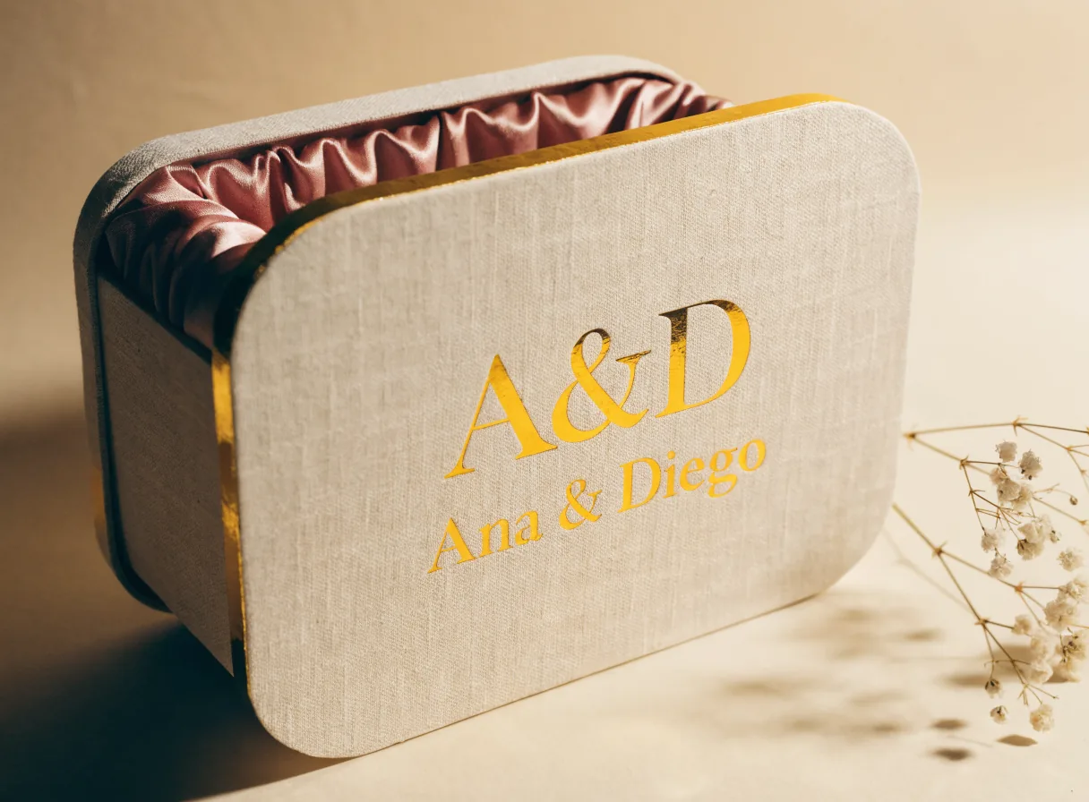 caja de regalo de lino hueso con el monograma A&D y el nombre Ana y Diego en foil dorado, con forro de satín rosa