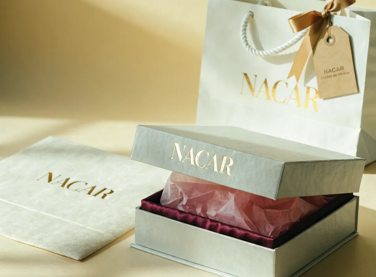 caja rígida crema con pañuelo magenta, bolsa con listón dorado y sobre, todo con la marca NACAR