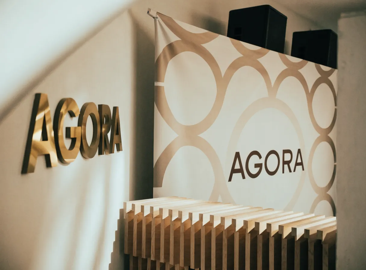 letras corpóreas AGORA en latón sobre un muro y un panel calado con el mismo emblema, la señalización de un espacio