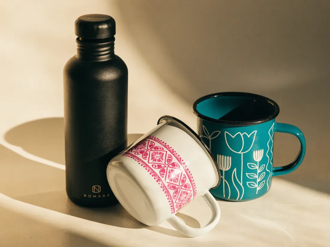botella negra de acero con dos tazas de peltre, una crema con grecas y una teal con tulipanes