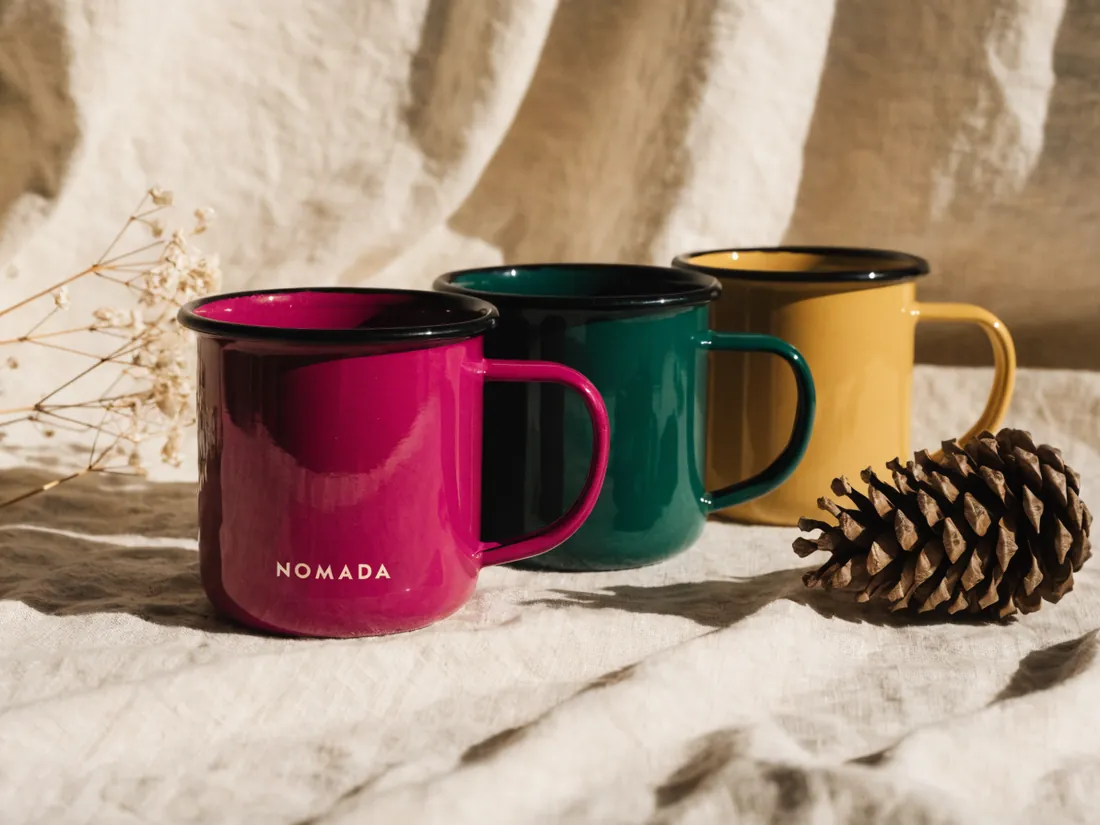 tres tazas de peltre en magenta, verde y mostaza junto a una piña sobre lino