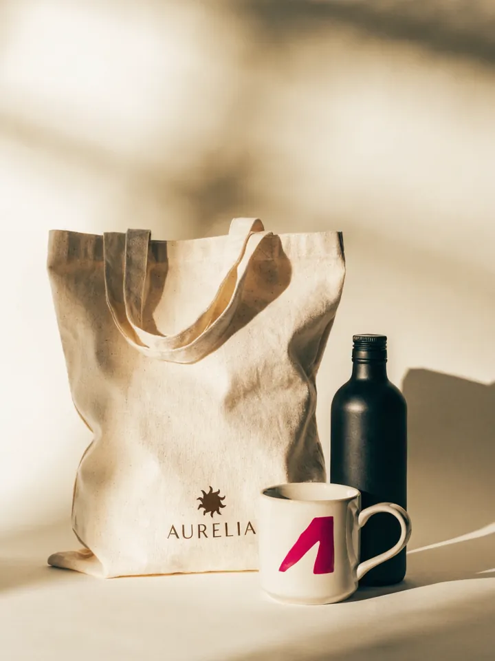 Tote de algodón crudo, botella negra y taza esmaltada con la marca AURELIA, el merchandising de una misma casa